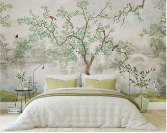 May include: A white bed with a green duvet cover and two green pillows. The bed is in front of a wall with a mural of a tree with white flowers and birds. The mural is painted in a watercolor style.