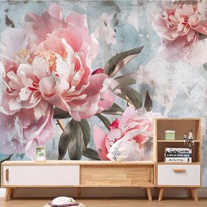 Op de afbeelding: Een bloemenmuurschildering met een verweerde, vintage uitstraling. De muurschildering toont grote roze pioenen met groene bladeren tegen een lichtblauwe achtergrond.