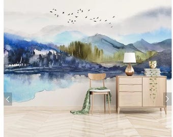 May include: A watercolor painting of a mountain landscape with a lake in the foreground. The painting is in shades of blue, green, and white. There is a wooden dresser with a lamp and a chair in the foreground.