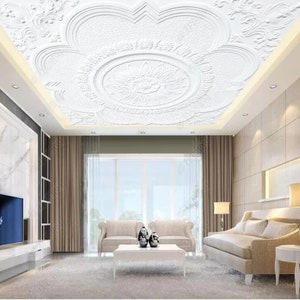 Könnte beinhalten: Eine weiße Decke mit einem dekorativen, dreidimensionalen Blumendesign. Die Decke befindet sich in einem Wohnzimmer mit beigefarbenen Wänden, einem großen Fenster und Möbeln.