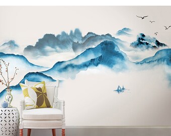 May include: A watercolor painting of blue mountains with white clouds and a small sailboat in the distance. The painting is on a white wall with a white chair and a small table in the foreground.