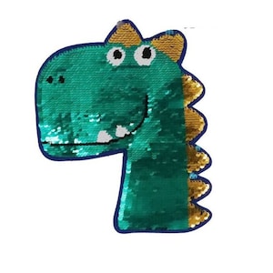 Könnte beinhalten: Grün-goldene Pailletten-Dinosaurierkopf-Applikation mit einem lächelnden Gesicht.