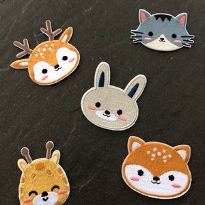 Könnte beinhalten: Fünf gestickte Bügelbilder mit niedlichen Tiergesichtern. Die Patches sind in verschiedenen Farben, darunter Braun, Grau und Gelb. Die Tiere umfassen ein Reh, eine Katze, ein Kaninchen, eine Giraffe und einen Fuchs.