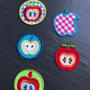 Könnte beinhalten: Fünf gestickte Apfel-Patches in verschiedenen Farben und Mustern. Die Patches sind rund und zeigen einen roten Apfel mit grünem Stiel und Blatt. Die Patches sind perfekt, um Kleidung, Taschen oder anderen Bastelarbeiten einen Hauch von Verspieltheit zu verleihen.
