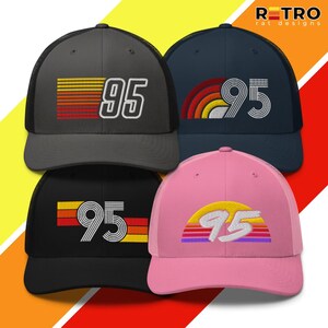 Peut inclure: Quatre casquettes de camionneur de couleurs variées : gris, bleu marine, noir et rose. Chaque casquette affiche le chiffre "95" en blanc, avec un design rétro. Les motifs comprennent des rayures et un arc-en-ciel, évoquant une esthétique vintage.