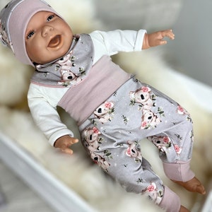 Könnte beinhalten: Ein Baby trägt ein graues und rosa Outfit mit Koala-Druck. Das Outfit besteht aus einem Langarmshirt, einer Hose und einer Lätzchen. Das Baby trägt eine rosa Strickmütze.