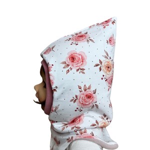 Könnte beinhalten: Weißer Kapuzen-Halswärmer mit rosafarbenem Blumenmuster und weißen Punkten. Der Halswärmer ist aus weichem Stoff gefertigt und hat ein rosa Fleecefutter.