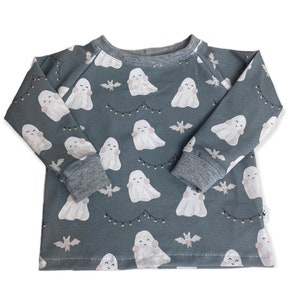 Könnte beinhalten: Ein langärmeliges, graues Shirt mit einem sich wiederholenden Muster aus freundlichen weißen Geistern, Fledermäusen und Lichterketten. Das Shirt hat einen grauen Rundhalsausschnitt und Manschetten. Dieses Halloween-Shirt ist für Kinder geeignet.