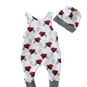 Puede incluir: Mono blanco para bebé con estampado de mariquita y gorro a juego. El mono tiene un diseño sin mangas y un ribete gris alrededor del cuello, los brazos y las piernas. El gorro es de estilo beanie con un borde gris.