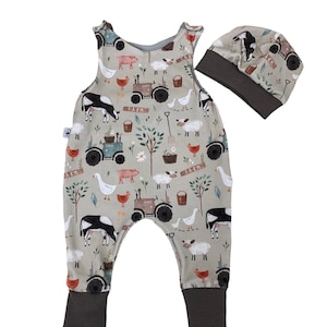 Könnte beinhalten: Ein grauer und grüner Baby-Overall mit einem Bauernhof-Tierdruck. Der Overall ist ärmellos und zeigt einen Traktor, Kühe, Schweine, Schafe und Gänse. Er wird mit einer passenden grauen und grünen Mütze geliefert.