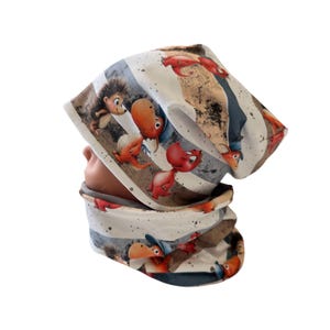 Puede incluir: Un conjunto de gorro y braga de cuello a rayas blancas y grises con ilustraciones de animales de dibujos animados. El gorro y la braga de cuello presentan un patrón repetido de animales de dibujos animados en rojo, marrón y azul. El conjunto es de material suave.