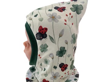 Puede incluir: Un gorro blanco con capucha y forro de borreguito verde. El gorro tiene un patrón de mariquitas, tréboles de cuatro hojas y flores.