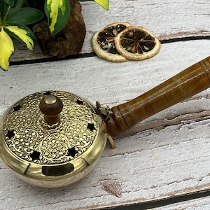 May include: A brass incense burner with a wooden handle. The burner has a decorative floral design and a small wooden knob on the top.