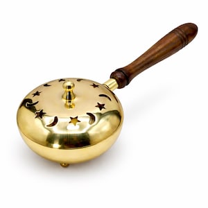 May include: A gold-colored incense burner with a wooden handle. The round burner features star and crescent moon cutouts on the lid. The handle is made of dark brown wood and is attached to the burner with a brass fitting.