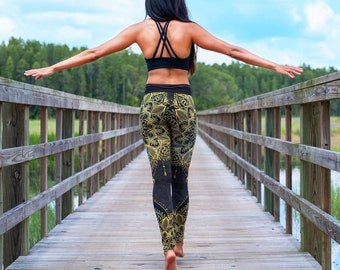 Pode incluir: Um top desportivo preto com design de alças nas costas e leggings de cintura subida com um padrão floral de mandala em preto e dourado. As leggings têm uma silhueta justa que vai até aos tornozelos, combinadas com um top desportivo preto.