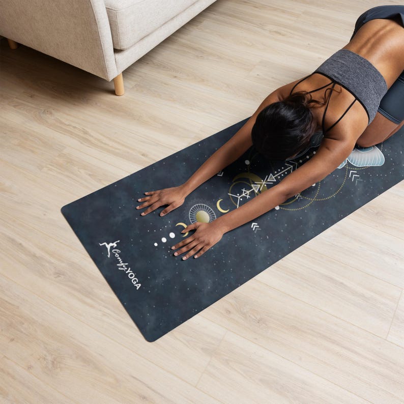 Pode incluir: Um tapete de ioga azul escuro com um design celestial com luas, estrelas e formas geom&eacute;tricas. O tapete tem as palavras "Comfy YOGA" impressas. Uma pessoa &eacute; mostrada em uma pose de ioga no tapete.