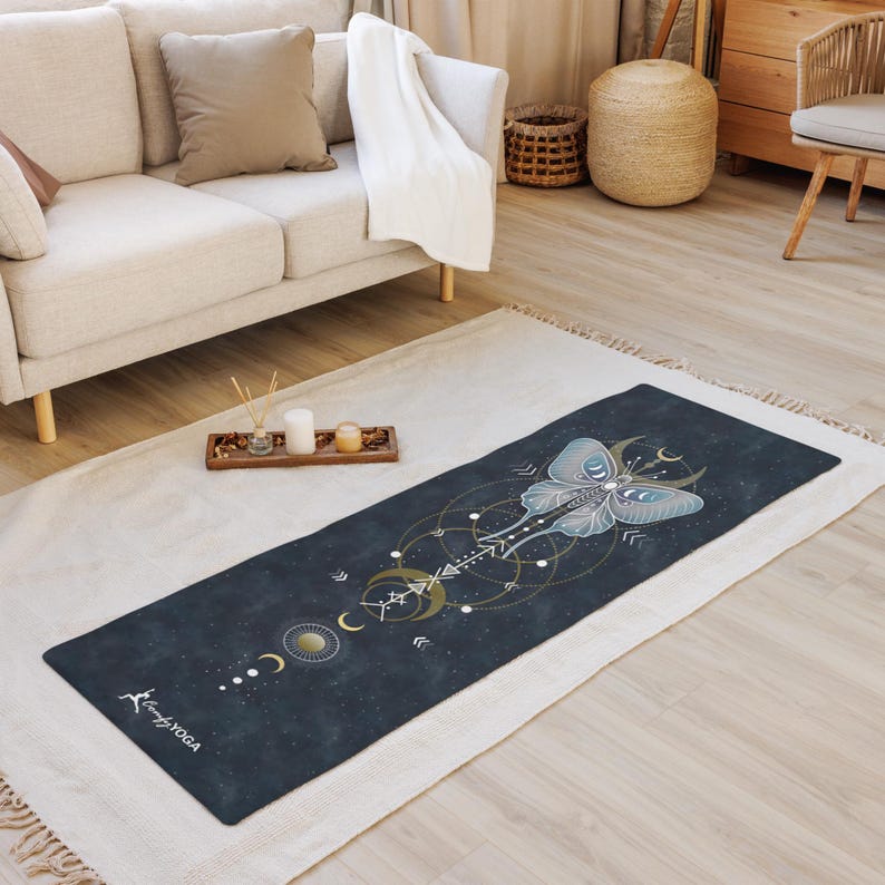 Pode incluir: Um tapete de ioga azul escuro com um desenho de mariposa celestial em azul claro e dourado. O tapete apresenta um padr&atilde;o geom&eacute;trico com luas e estrelas, e o texto "Comfy Yoga" &eacute; vis&iacute;vel em branco.