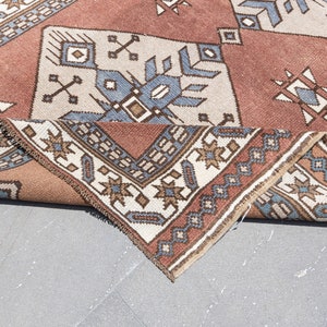 May include: A folded rug with a geometric pattern in shades of brown, blue, and white. The rug has a traditional design with intricate details.
