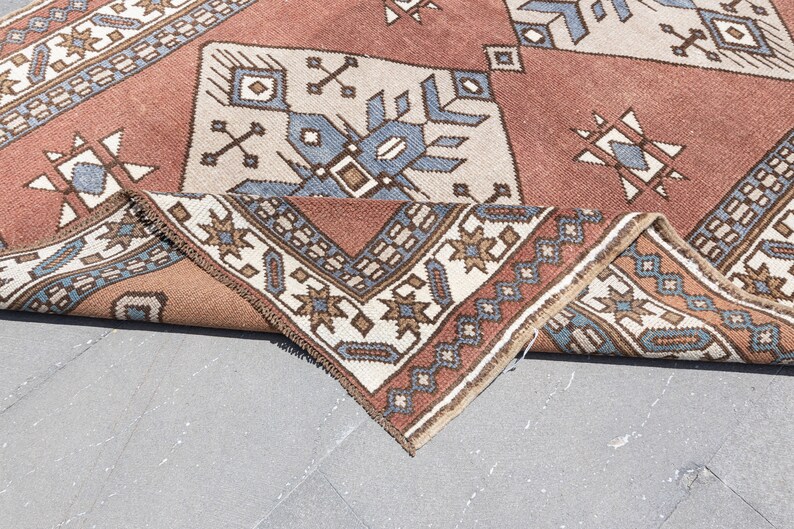 May include: A folded rug with a geometric pattern in shades of brown, blue, and white. The rug has a traditional design with intricate details.