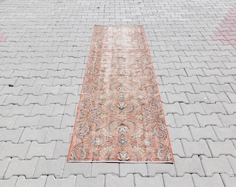 Puede incluir: Una alfombra de estilo vintage con un patrón floral en tonos rosa, naranja y marrón. La alfombra tiene un aspecto descolorido y desgastado y está colocada sobre una superficie de hormigón gris.