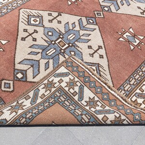 May include: Close-up of a folded rug with a geometric pattern in shades of brown, blue, and white. The rug has a traditional design with intricate details.