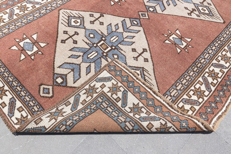 May include: Close-up of a folded rug with a geometric pattern in shades of brown, blue, and white. The rug has a traditional design with intricate details.