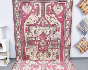 May include: A vintage Turkish rug with a pink and cream color scheme. The rug features a geometric pattern with intricate details. The rug is in good condition and has a worn look.