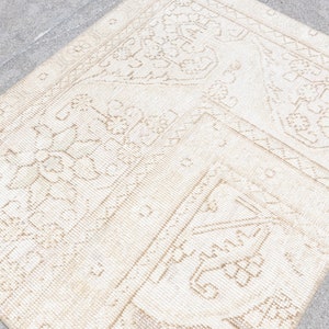 May include: A white rug with a beige pattern of intricate floral designs. The rug has a worn, vintage look.