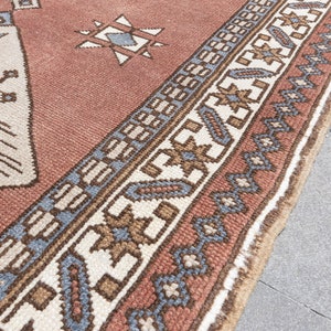 May include: A close-up of a red, white, and blue patterned rug with a fringe border. The rug has a geometric design with a central diamond shape.