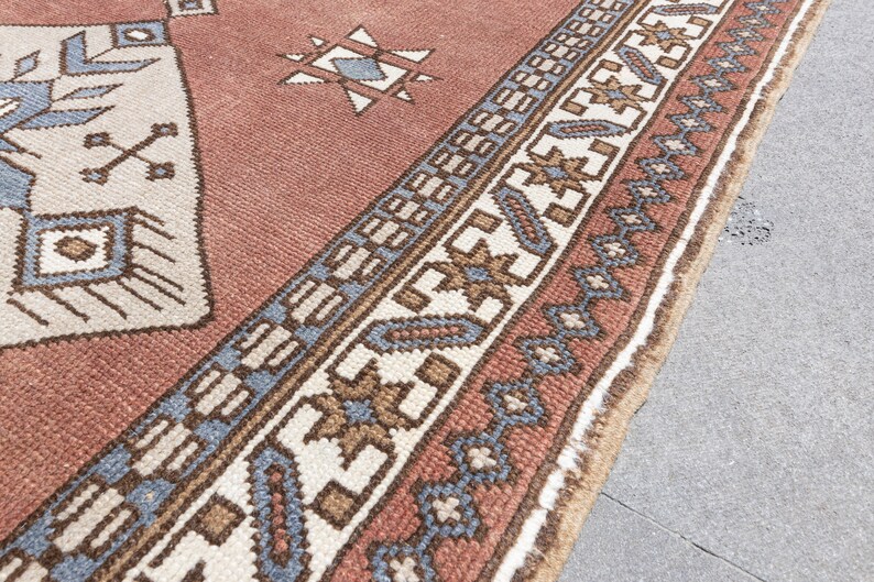 May include: A close-up of a red, white, and blue patterned rug with a fringe border. The rug has a geometric design with a central diamond shape.