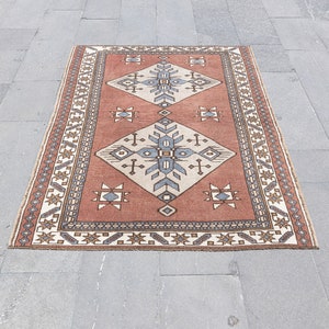 May include: A traditional rug with a geometric pattern in shades of red, brown, white, and blue. The rug has a border with a repeating pattern.