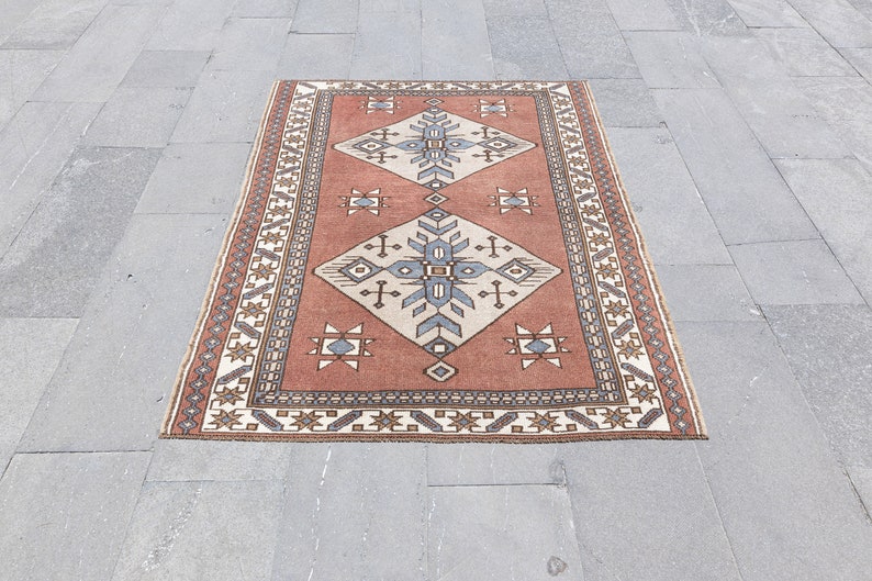 May include: A traditional rug with a geometric pattern in shades of red, brown, white, and blue. The rug has a border with a repeating pattern.