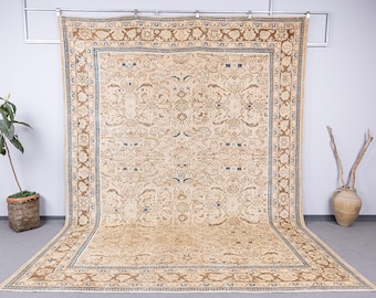 May include: Large, rectangular beige rug with an intricate floral pattern. The rug has a brown border with a blue accent and is displayed against a neutral background. A decorative piece for any room.