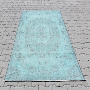 Puede incluir: Una alfombra vintage azul turquesa con un patrón floral descolorido. La alfombra tiene un aspecto desgastado y está hecha de un material suave y tejido.