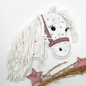 Può includere: Applique per la testa di cavallo in feltro bianco con briglia glitter rosa e criniera in filato bianco. L'applique è su uno sfondo bianco con una stella rosa ed erba secca.