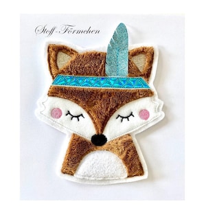 Könnte beinhalten: Ein brauner Plüschfuchs mit einem blauen und weißen Kopfschmuck und einer Feder. Der Fuchs hat geschlossene Augen und eine rosa Nase.