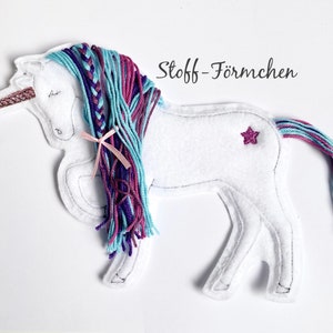 Può includere: Unicorno di feltro bianco con una lunga criniera intrecciata e una coda di lana blu, viola e rosa. L'unicorno ha una stella rosa sulla schiena e il testo "Stoff - Förmchen" sopra.