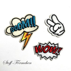 Könnte beinhalten: Drei gestickte Bügelbilder mit weißem Hintergrund. Ein Patch zeigt eine blaue Wolke mit dem Wort "BOOM!" in Weiß. Ein weiterer Patch zeigt eine rote Sprechblase mit dem Wort "WOW!" in Weiß. Der letzte Patch zeigt eine weiße Hand, die ein Peace-Zeichen macht.