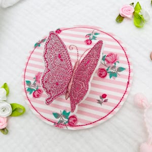 May include: A pink glitter butterfly applique on a pink and white striped fabric with a floral pattern.