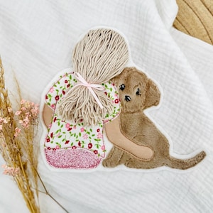 Op de afbeelding: Een geborduurde patch met een meisje dat een puppy omhelst. De rug van het meisje is zichtbaar, met een bloemenjurk en een paardenstaart vastgebonden met een roze strik. De puppy is bruin met een lieve uitdrukking. De patch staat op een witte achtergrond.