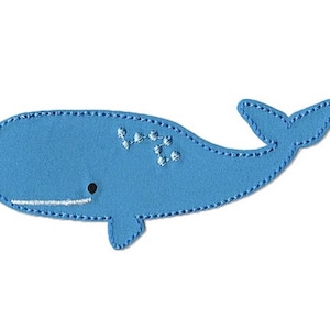 Può includere: Un'applicazione di balena in feltro blu con cuciture bianche. La balena ha un piccolo occhio e una bocca con una linea bianca.