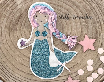 May include: A blue and teal mermaid with pink and purple hair holding a purple starfish. The mermaid is embroidered on a wooden surface with pink stars and white circles.