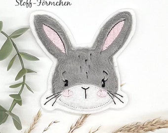 Könnte beinhalten: Ein grauer Filz-Hasen-Applik mit rosa Ohren und einem weißen Gesicht. Die Applikation hat gestickte Details für die Augen, die Nase und die Schnurrhaare.