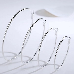 May include: Four silver hoop earrings of varying sizes are displayed against a white background. The earrings are simple, round, and made of a shiny, reflective metal. The hoops are arranged in a diagonal line, showcasing their graduated sizes.
