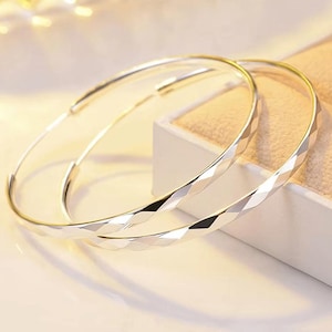 May include: A pair of large silver hoop earrings featuring a faceted, diamond-cut texture along the outer surface. The circular earrings have a polished, reflective finish that catches the light, creating a bright, metallic appearance.