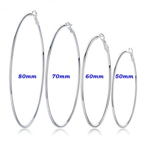 May include: Four silver hoop earrings in varying sizes: 80mm, 70mm, 60mm, and 50mm. The earrings are displayed against a white background, with the measurements in blue text. The hoops are simple and shiny, reflecting light.