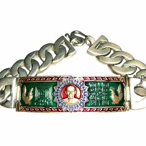 May include: A silver-toned metal chain bracelet featuring a central rectangular plaque with a green enamel background. The plaque displays a central circular portrait of a person, flanked by two golden rooster figures and intricate engraved symbols.