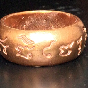 May include: A gold ring with an inscription in an unknown language. The ring is thick and has a rounded shape.