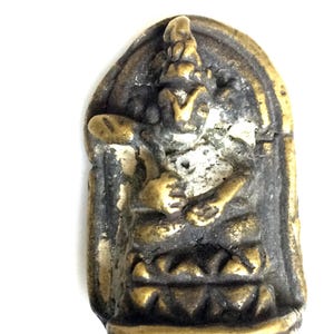 Puede incluir: Pequeña figura de latón envejecido que representa una deidad sentada. La figura está en posición sentada, con detalles intrincados visibles. El fondo es una forma oscura y arqueada.