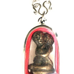 May include: A silver chain necklace with a silver and red pendant featuring a small bronze statue of two figures embracing.